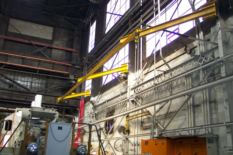 Yellow wall-mounted jib arms carrying rigid rail in a locomotive repair shop