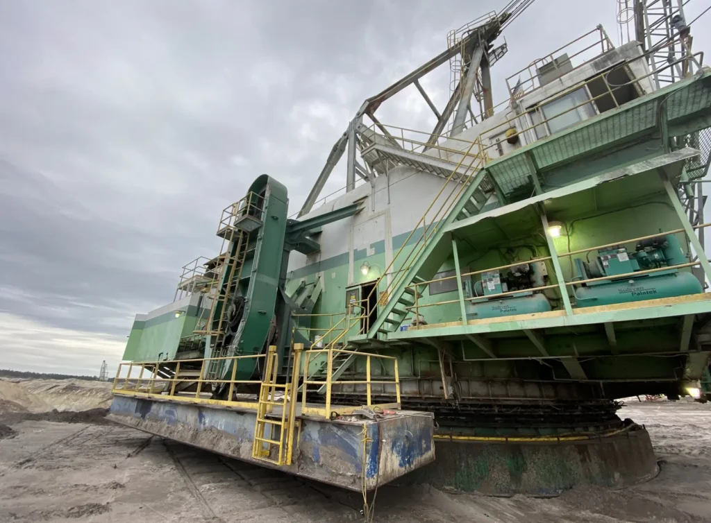 Large open-pit mining machine with elevated walkways and guardrail on its superstructure under an overcast sky