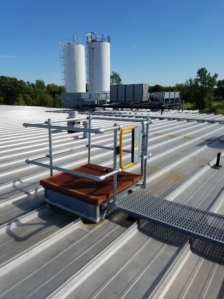 Galvanized guardrail and a self-closing gate around a roof hatch with a grated walkway on a metal roof